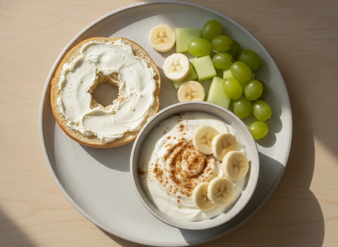 Bagel with cream cheese, yogurt bowl with banana, and fresh fruit photo